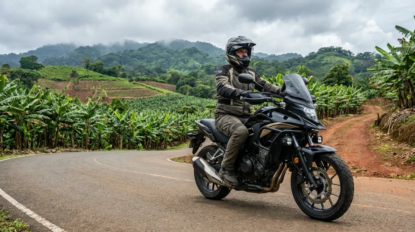 Motociclista con casco integral y chaqueta recorriendo en una moto adventure negra una carretera rural de Panamá que se convierte en camino de tierra entre plantaciones de banano